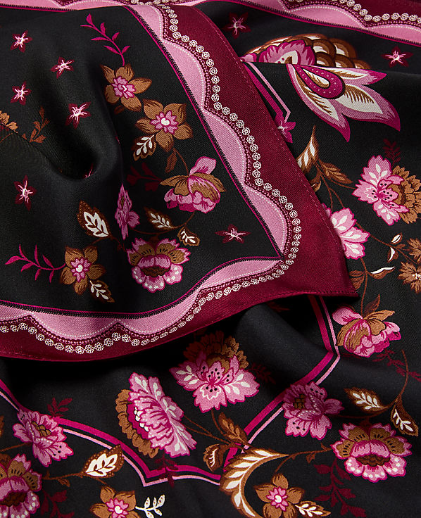 A close-up view of a black fabric with a vibrant floral pattern in shades of pink and brown, featuring a scalloped border.