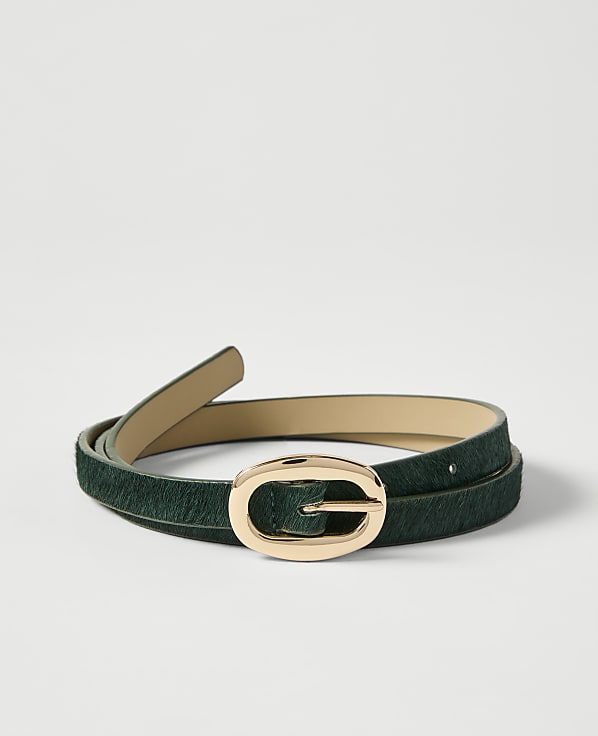 A dark green, textured belt with a gold oval buckle lies coiled on a plain white background.