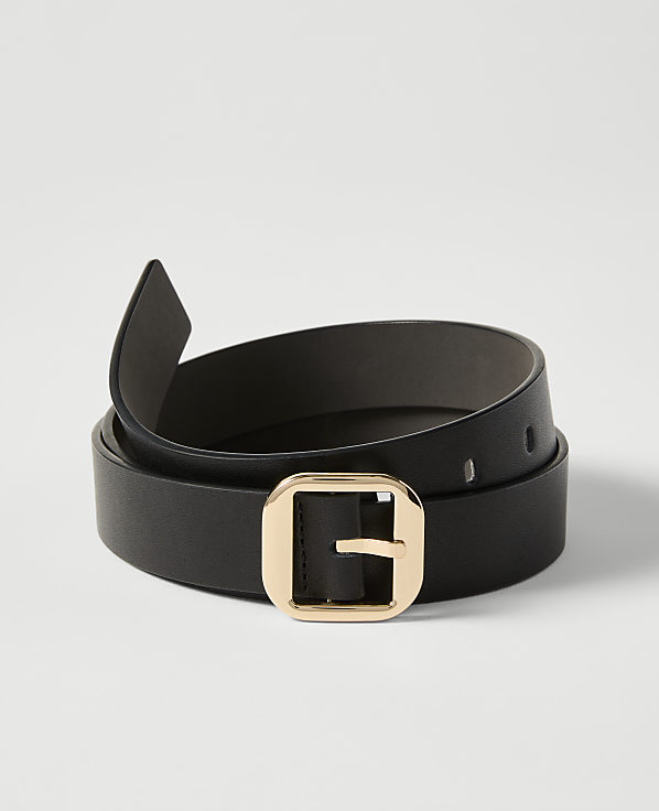 A black leather belt with a gold buckle is coiled on a plain white background.
