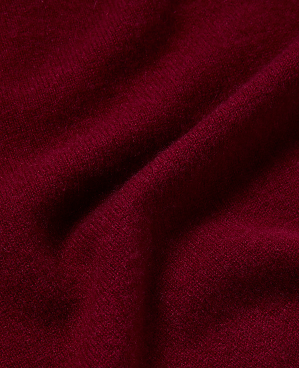 Deep red fabric with soft folds and subtle texture fills the frame, with shadows creating depth in the background.
