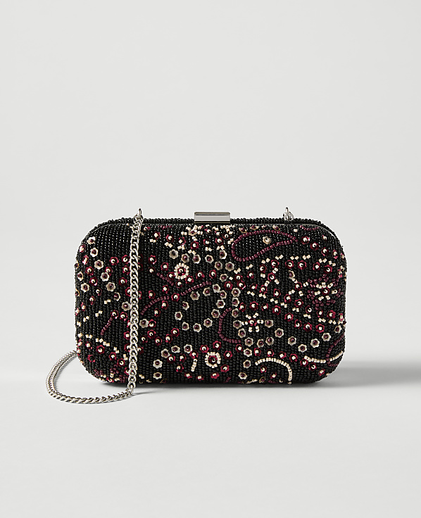 A black beaded clutch with a floral pattern and a silver chain rests against a plain white background.