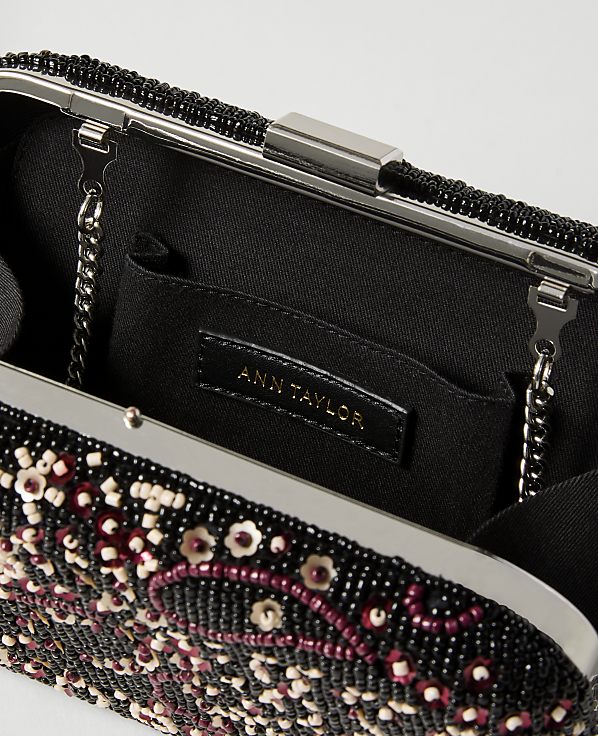 A black beaded clutch with a floral design in the foreground is open to reveal a black interior with an Ann Taylor label in the background.
