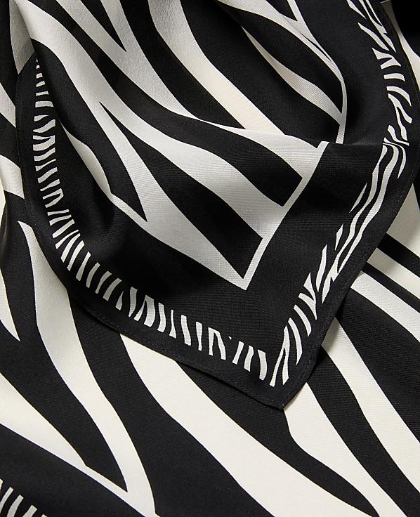 A black and white zebra-print scarf with a decorative border is laid out against a matching patterned background.