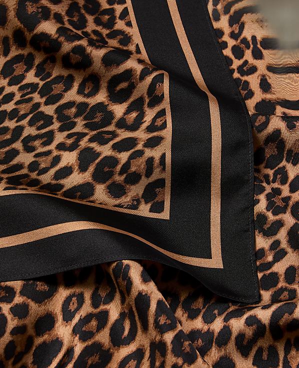 A close-up of a leopard print scarf with a black and tan border is draped over a matching fabric.