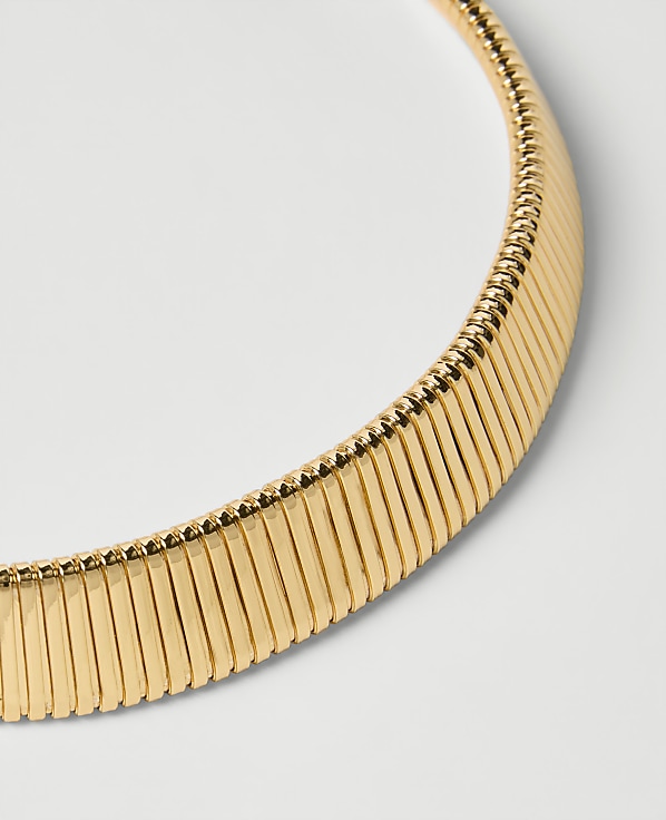 A close-up of a gold omega necklace with a white background.
