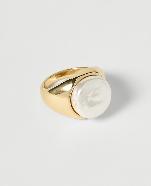A gold ring with a large, irregular pearl sits on a plain white surface.