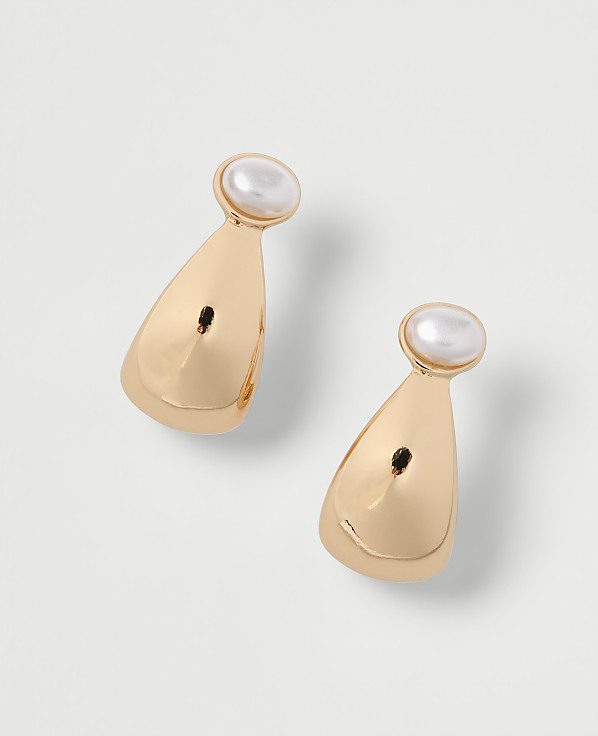 A pair of gold teardrop earrings with pearl accents rests on a plain white background.