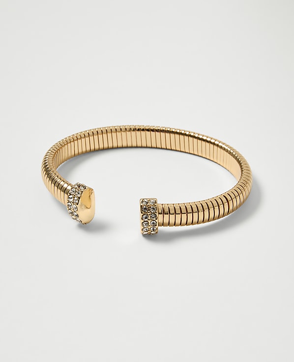 A gold, flexible bracelet with jeweled ends rests on a plain white background.