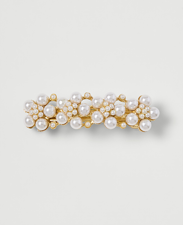 A gold barrette adorned with clusters of pearls sits on a plain, light-colored background.