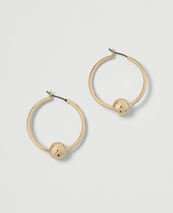 A pair of gold hoop earrings with a single bead on each rests on a plain white background.