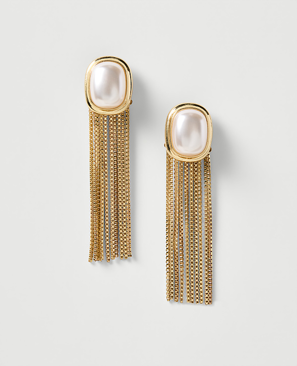 A pair of gold earrings with pearl tops and long, shimmering fringe hang against a plain, light background.