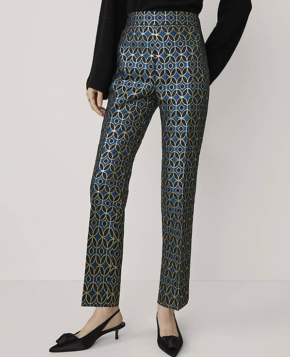 A person stands in the foreground wearing teal and gold patterned pants and black kitten heels, against a plain white background.