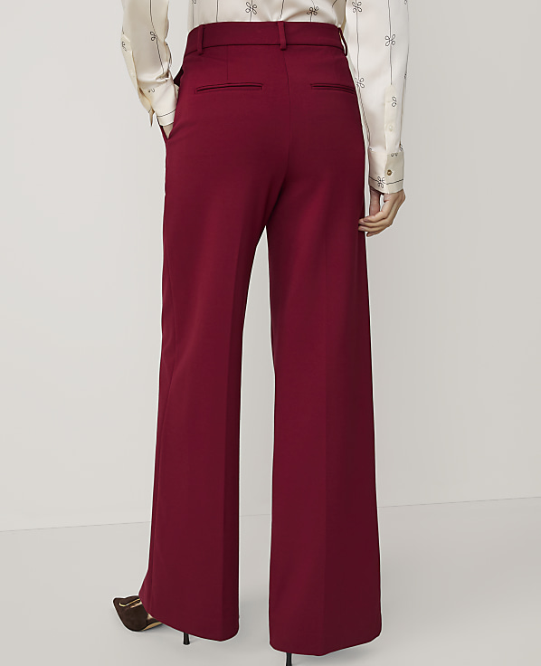 A person wearing wide-leg burgundy pants and a patterned blouse stands against a plain white background.
