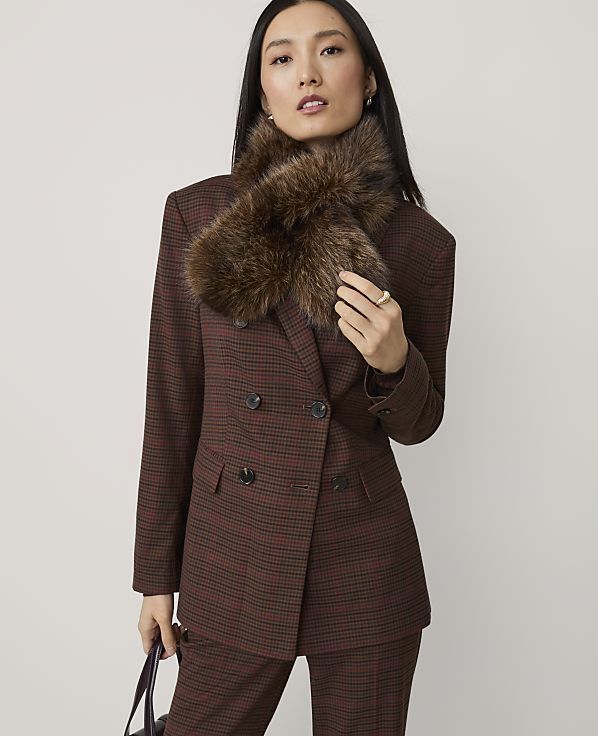 A woman in a brown plaid suit and fur collar stands against a plain gray background.