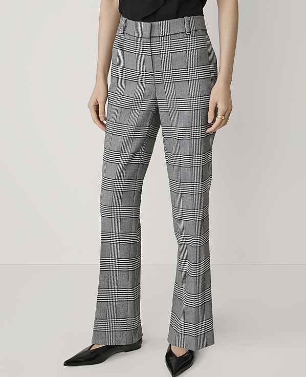 A person stands in front of a plain white background, wearing plaid flared trousers and black pointed-toe flats.