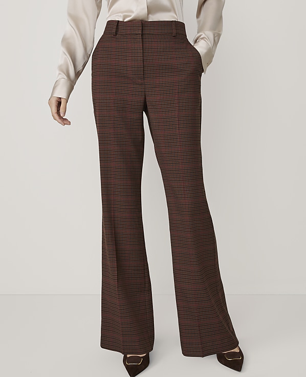 A person in a cream-colored silk blouse and brown plaid flared trousers stands against a plain white background.