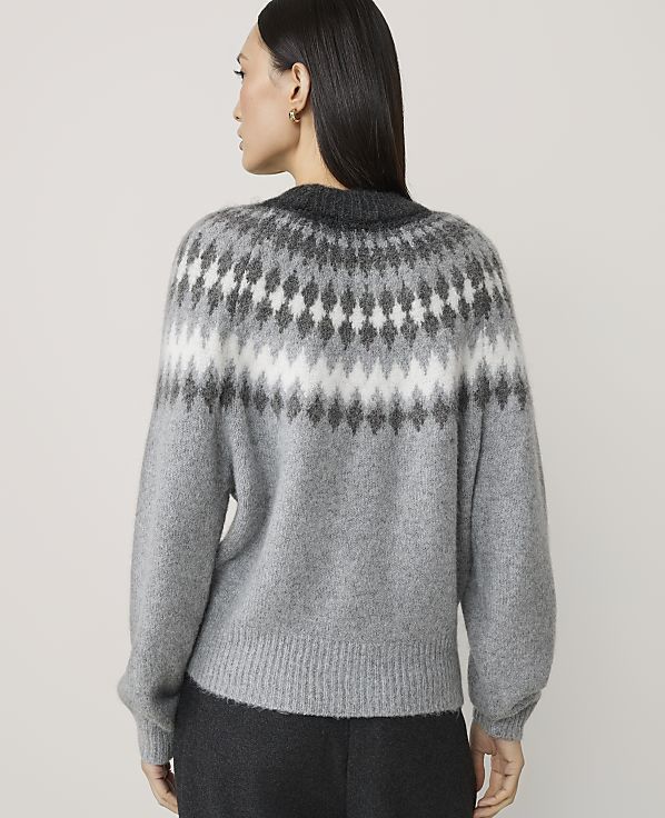 A woman in a grey sweater with a fair isle pattern stands against a plain white background.