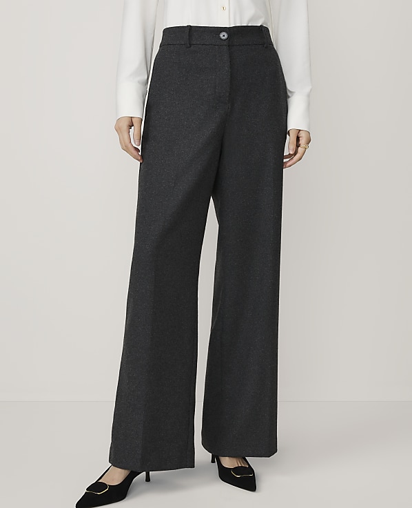A person in a white shirt and dark grey wide-leg trousers stands against a plain white background.
