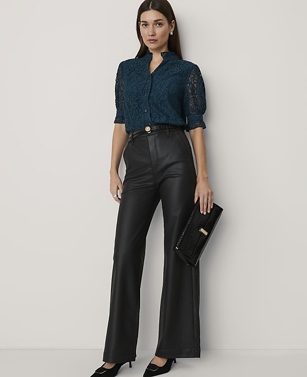 A woman in a teal lace blouse and black leather pants holds a black clutch against a plain white background.