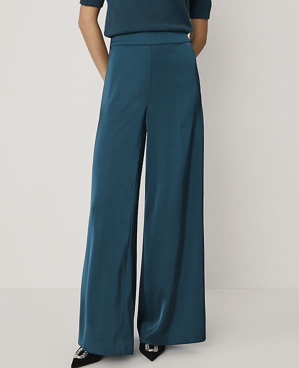 A person stands in teal wide-leg satin pants and a matching top against a plain white background.
