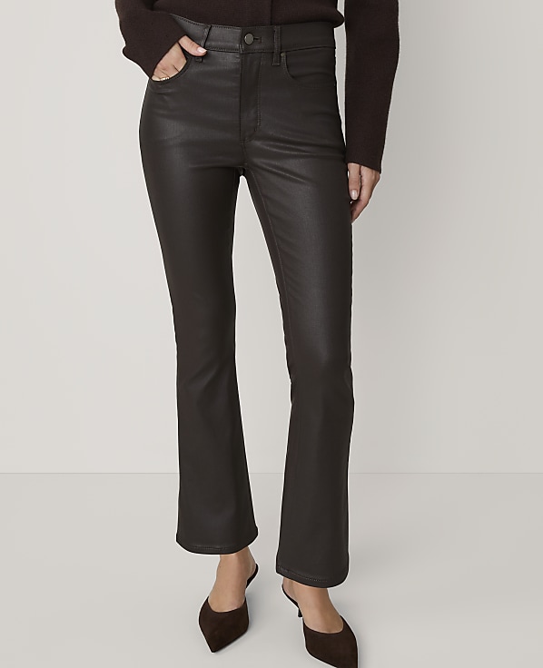 A person in dark brown, high-waisted, flared pants and brown mules stands against a plain, light brown background.