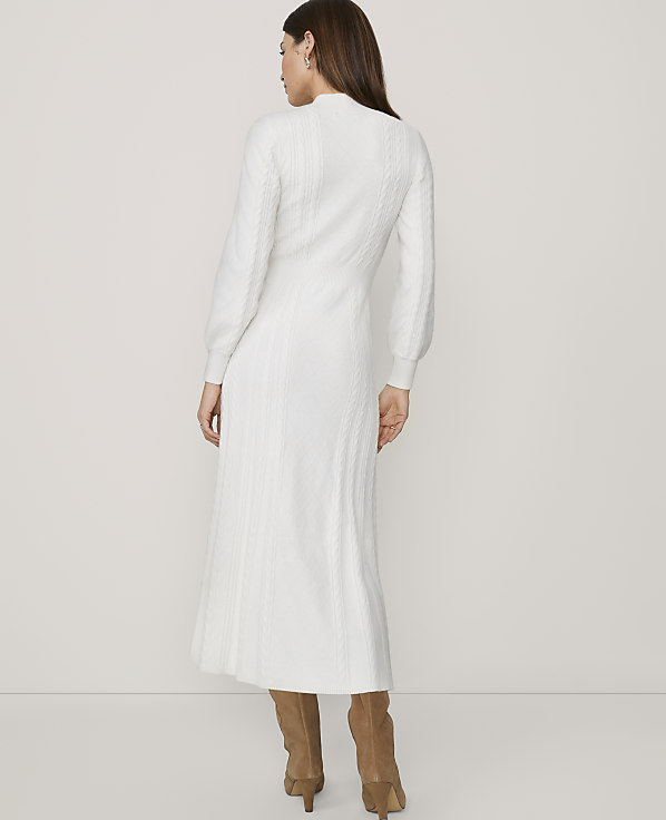 A woman in a white cable-knit dress and brown boots stands against a plain white background.