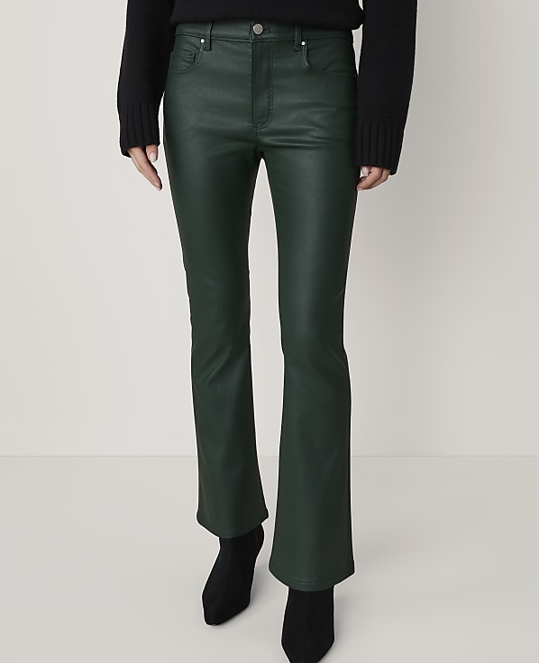 A person stands in dark green flared pants and black boots against a plain, light-colored background.