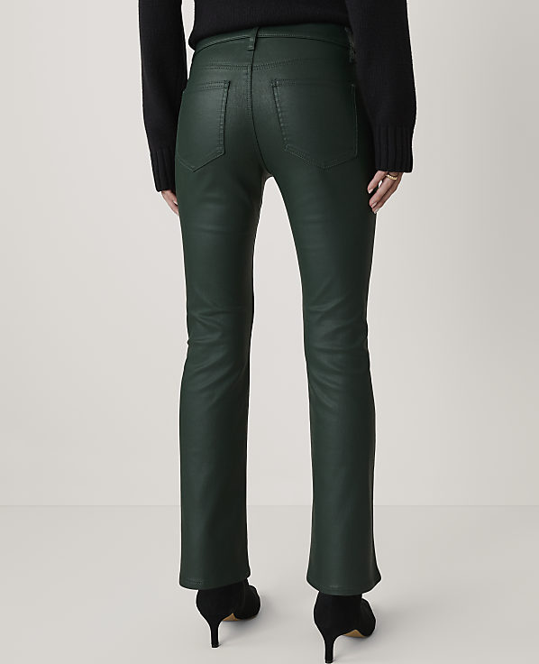 A person wearing dark green, flared pants and black heels stands against a plain white background.