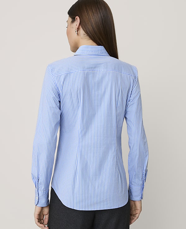 A woman in a blue and white striped button-down shirt stands against a plain, light-colored background.