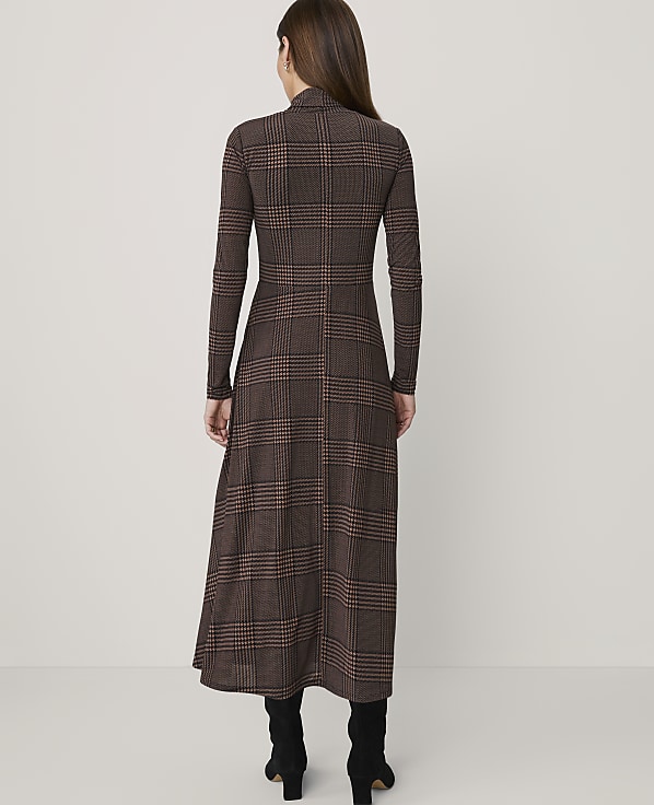 A woman in a brown plaid dress stands against a plain white background.
