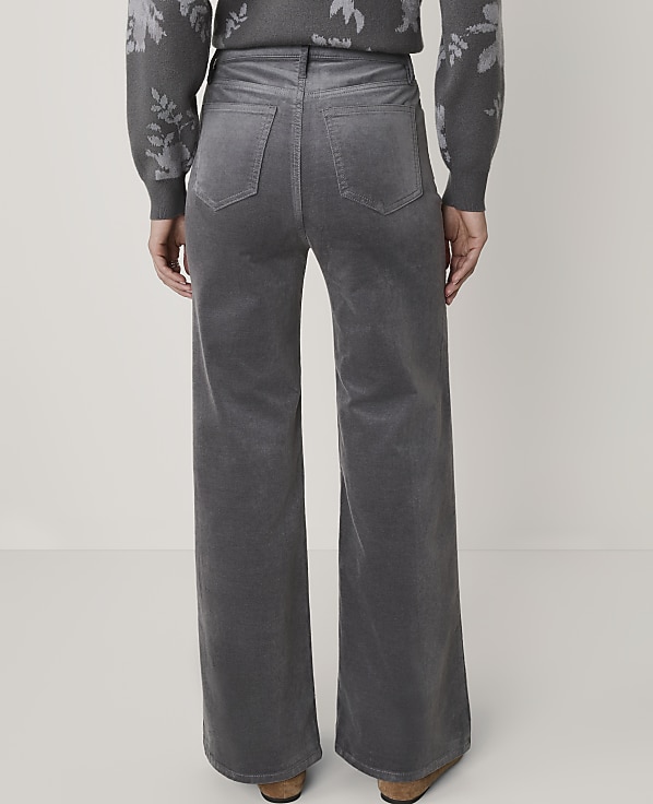 A person wearing gray corduroy wide-leg pants and a patterned sweater stands against a plain white background.