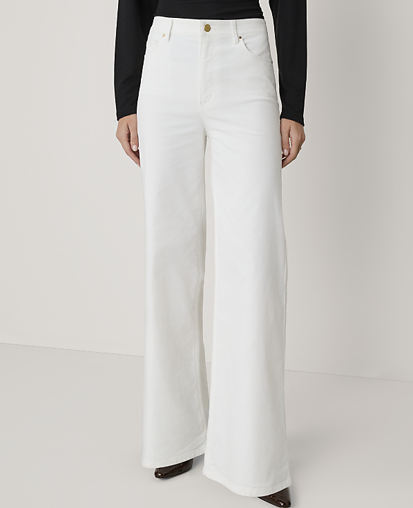 A person stands in white wide-leg jeans and a black top against a plain white background.