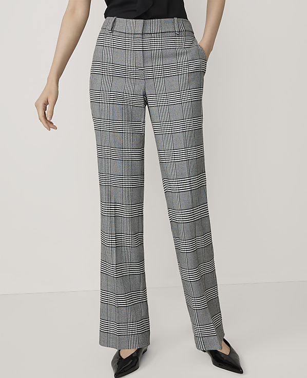 A person stands in the foreground wearing plaid trousers and black pointed-toe shoes against a plain white background.