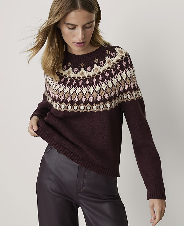 A woman in a burgundy sweater with a fair isle pattern stands against a plain white background.