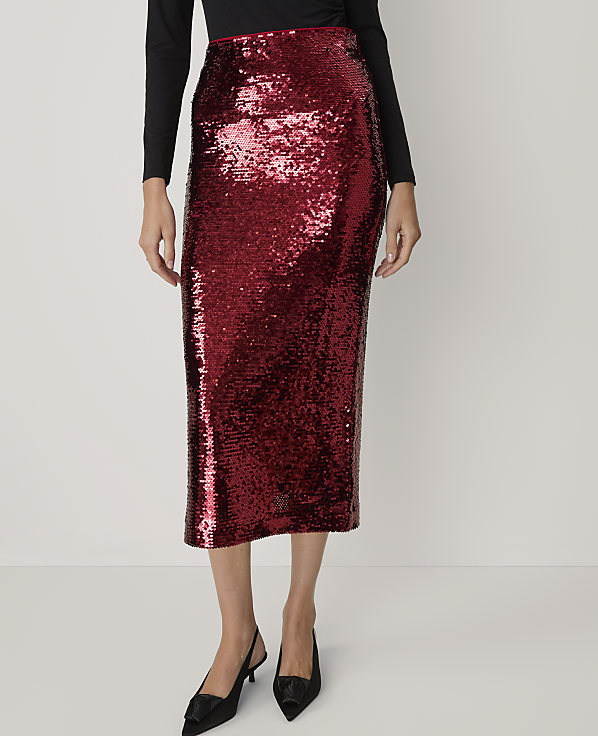 A person stands in a studio setting wearing a shimmering red sequined pencil skirt and black pointed-toe heels against a plain white background.