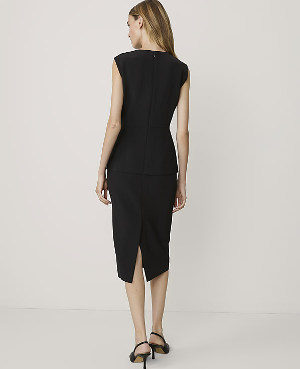 A woman in a black dress stands against a plain white background.