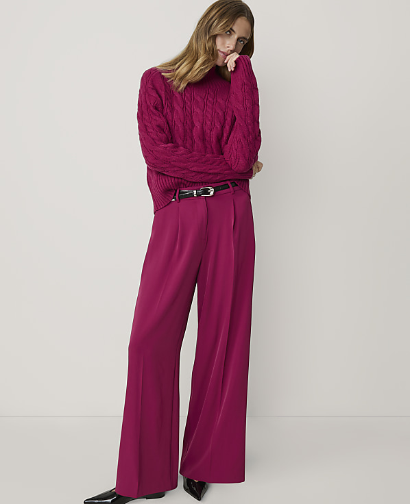 A woman in a magenta cable-knit sweater and matching wide-leg pants stands against a plain white background.