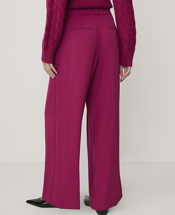 A person wearing a magenta sweater and matching wide-leg pants stands against a plain white background.