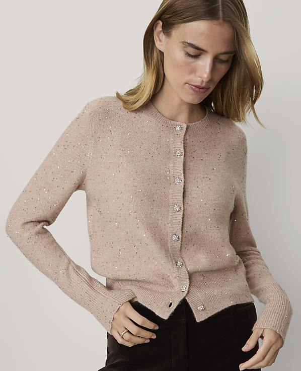 A woman in a sparkly pink cardigan stands against a plain white background.