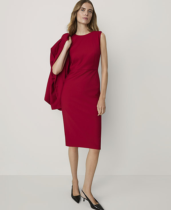 A woman in a red dress and black heels stands against a plain white background, with a red blazer draped over her shoulder.