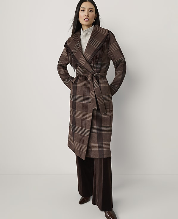 A woman in a brown plaid coat with fringe stands against a plain white background.