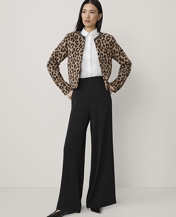 A woman in a leopard print cardigan and black wide-leg pants stands against a plain, light gray background.