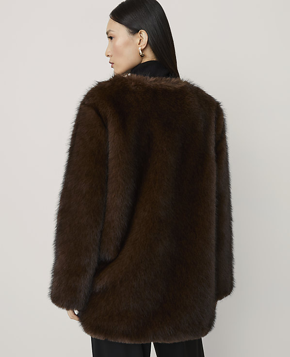 A woman in a brown faux fur coat stands against a plain white background.