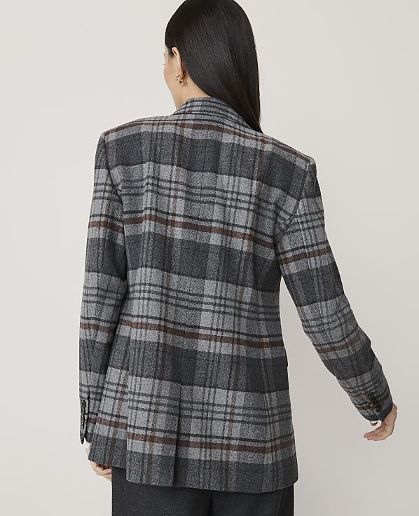 A woman in a gray plaid blazer stands against a plain, light gray background.