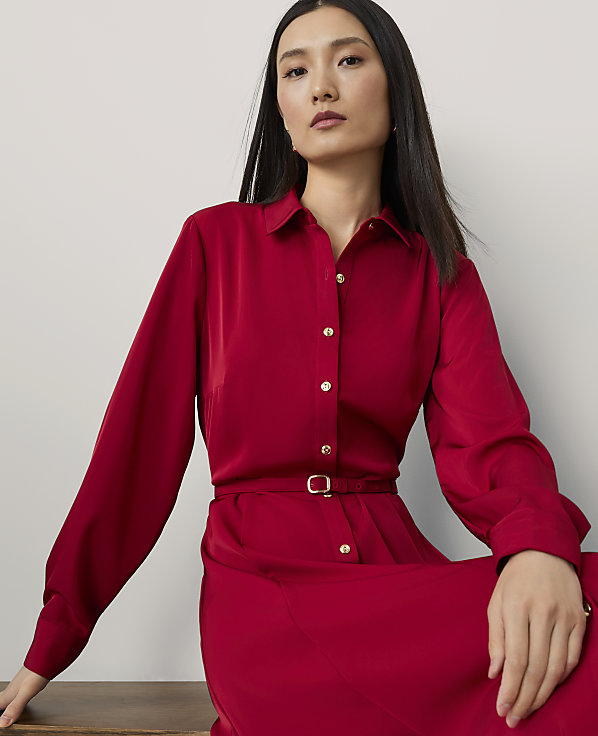 A woman in a red dress with a belted waist is seated against a plain, light-colored background.