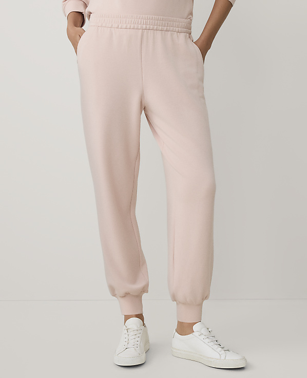 A person wearing light pink sweatpants and white sneakers stands against a plain, light-colored background.
