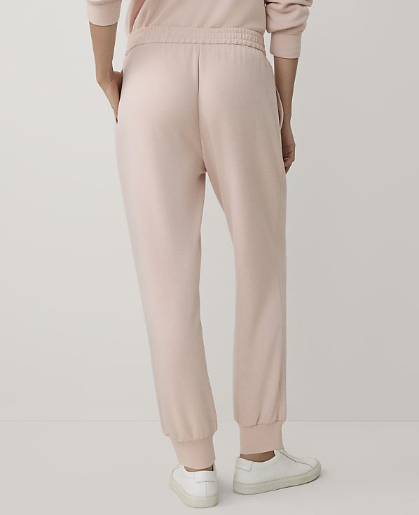 A person wearing light pink sweatpants and white sneakers stands against a plain white background.