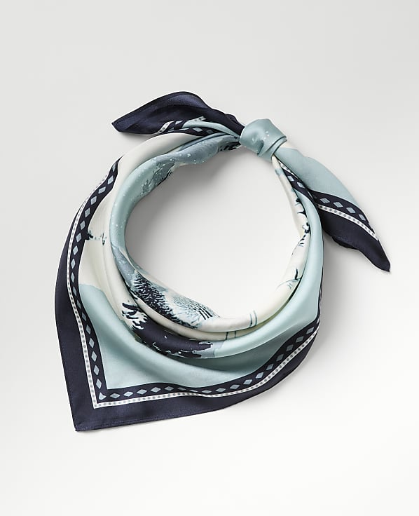 A blue and white patterned silk scarf is tied in a knot against a plain light gray background.