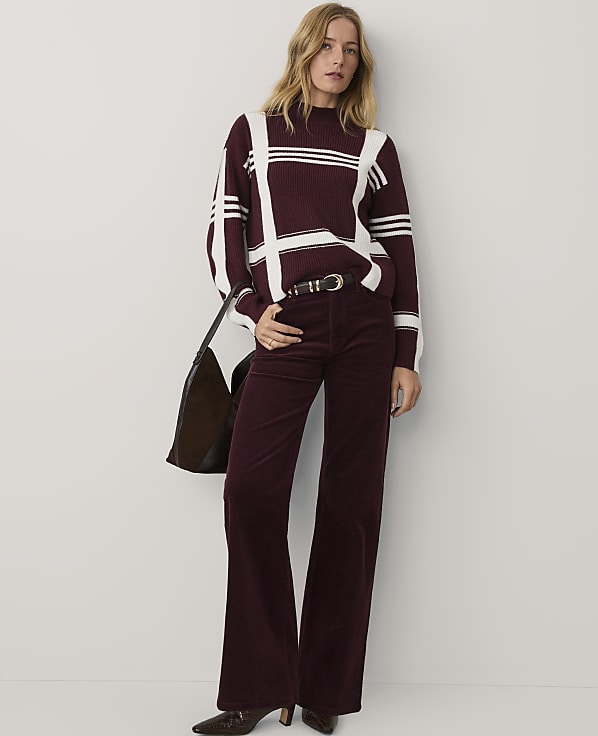 A woman wearing a burgundy and white striped sweater and matching flared trousers stands against a plain white background.