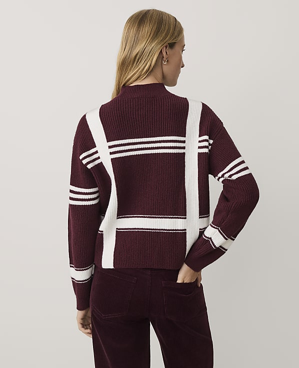 A woman wearing a burgundy and white plaid sweater and matching corduroy pants stands against a plain light gray background.